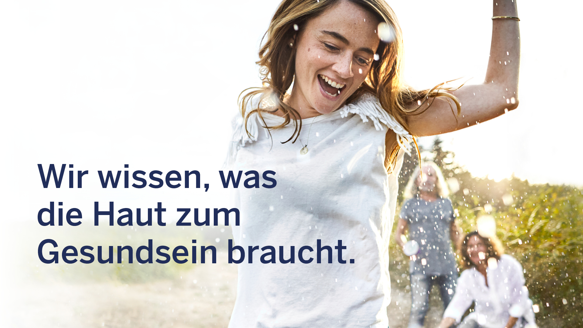Junge Frau tanzt fröhlich im Gegenlicht mit Wasser- und Lichteffekten, daneben Slogan: Wir wissen, was die Haut zum Gesundsein braucht