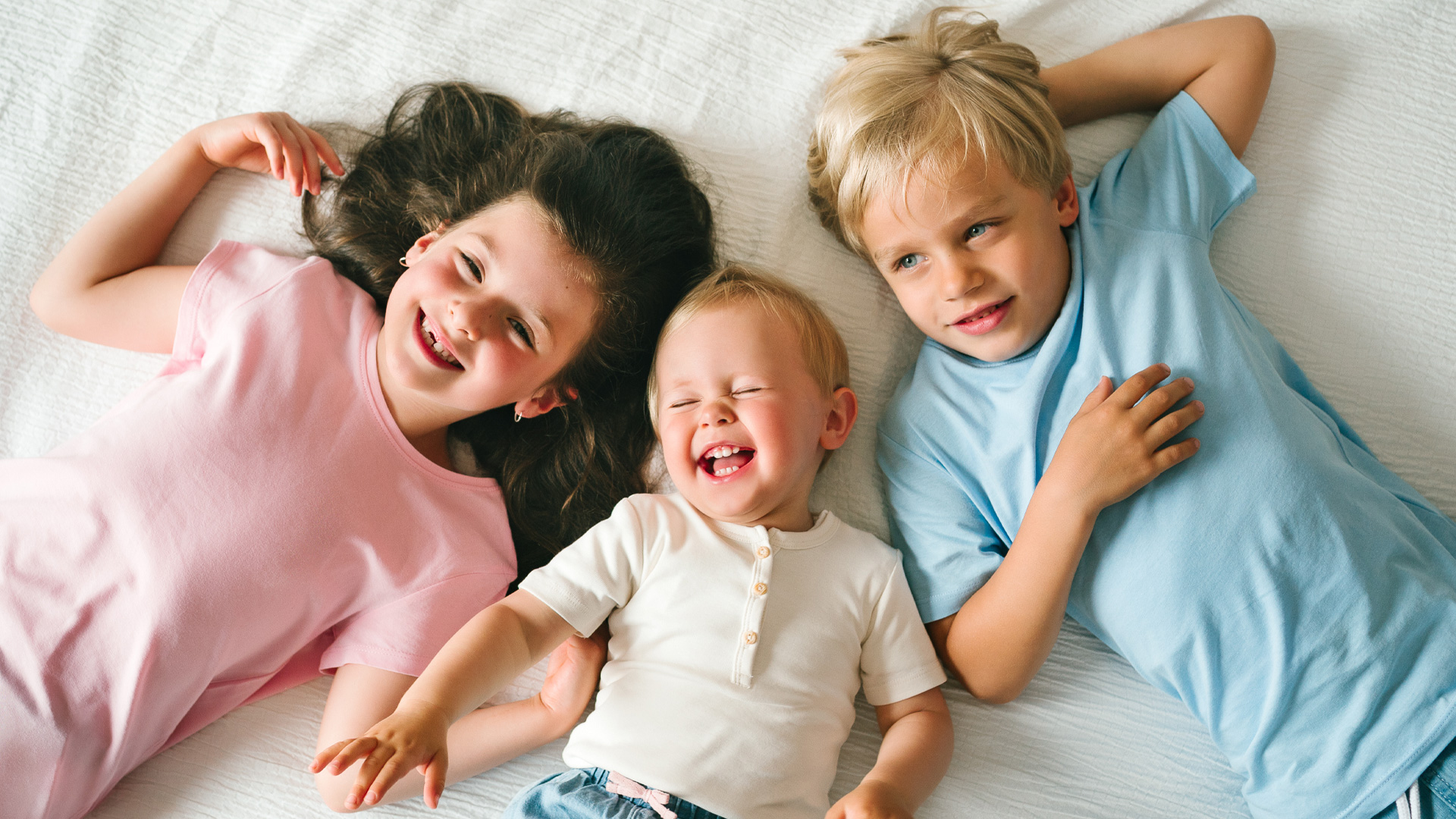 Drei Kleinkinder liegen aneinander gekuschelt und lachen